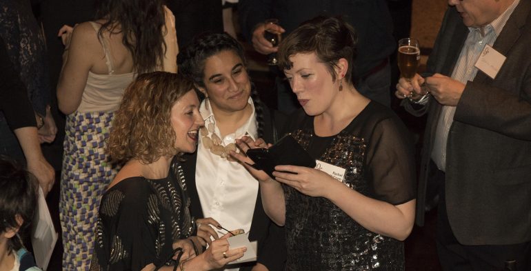 Three woman smiling while looking at an iPhone screen