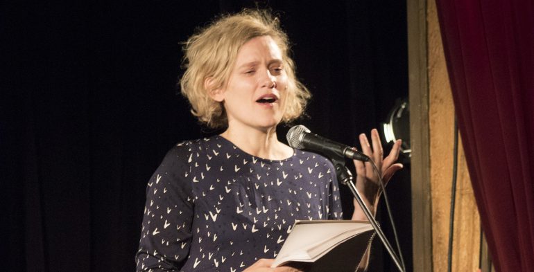 Young blond woman reading passionately at a microphone