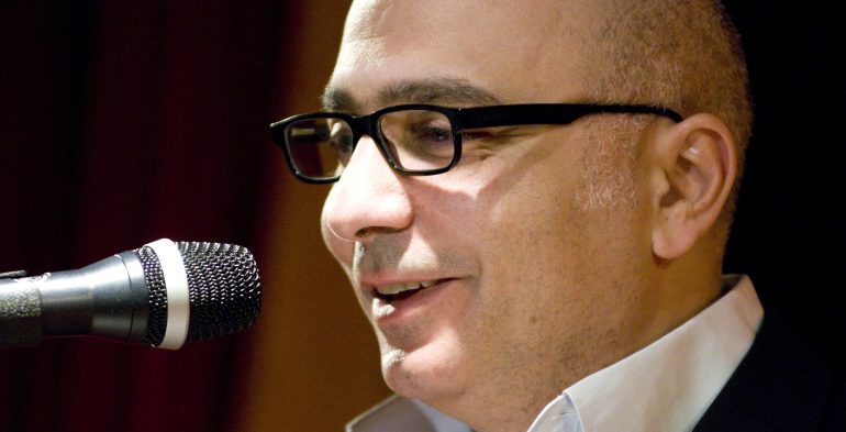 Man smiles as he speaks into the microphone